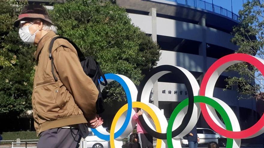 Un hombre protegido por mascarilla da la espalda a los anillos olímpicos instalados en Tokio