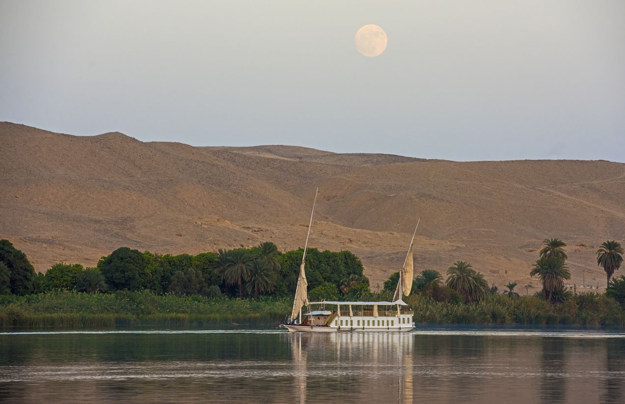 Dahabeya de lujo navegando por el río al atardecer con el reflejo de la luna en el cielo
