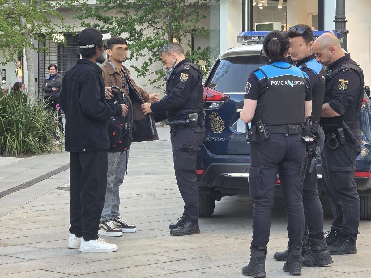 Efectivos de Policía Local y Policía Nacional identificando a dos peatones en la calle.
