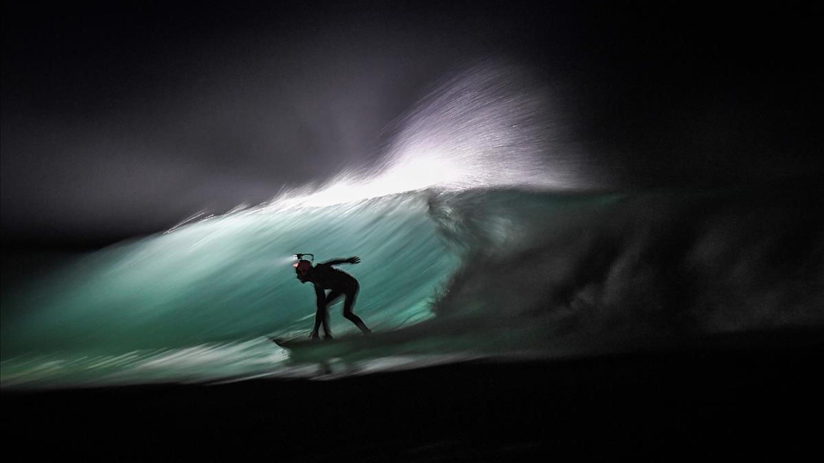 Un surfista nocturno con un potente faro a prueba de agua en la playa de Cap Frehel, en Plevenon, Gran Bretaña .