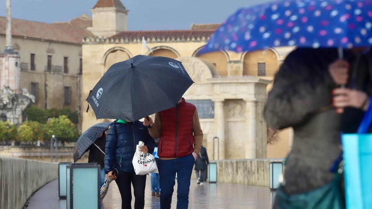 Viandantes se refugian de la lluvia con sus paraguas en el Puente Romano de Córdoba.