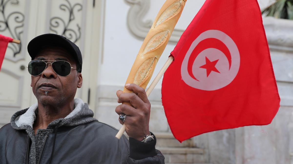 Un manifestante sostiene una barra de pan y una bandera de Túnez para protestar por el aumento del coste de la vida.