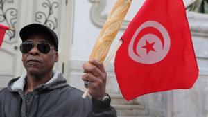 Un manifestante sostiene una barra de pan y una bandera de Túnez para protestar por el aumento del coste de la vida. 