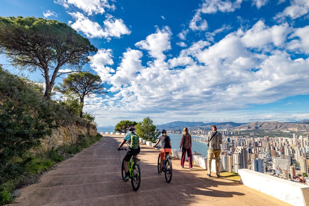 Dos ciclistas adelantan a una pareja en Sierra Helada. Debajo Benidorm