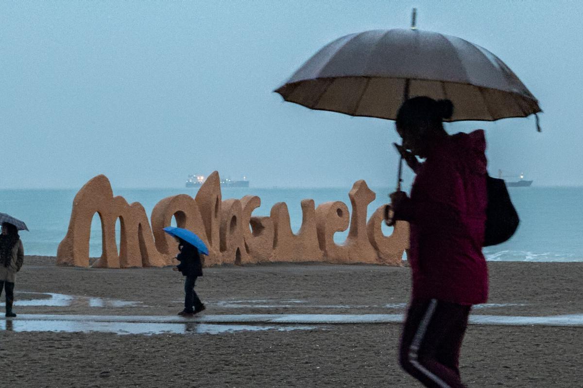 Varias personas se protegen de la lluvia en la playa la Malagueta, durante la borrasca Marta