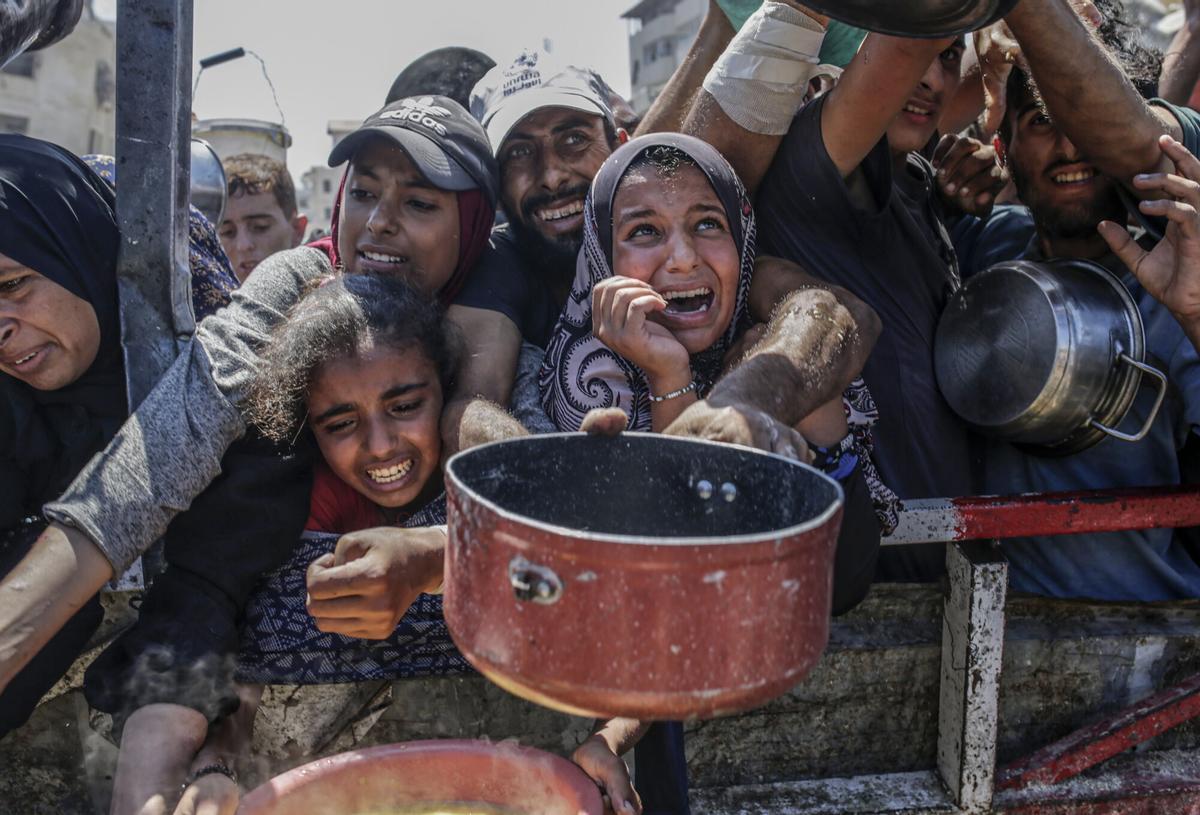 Palestinos desplazados internos, incluidos niños, sostienen ollas mientras se reúnen para recibir alimentos de un comedor benéfico en Gaza
