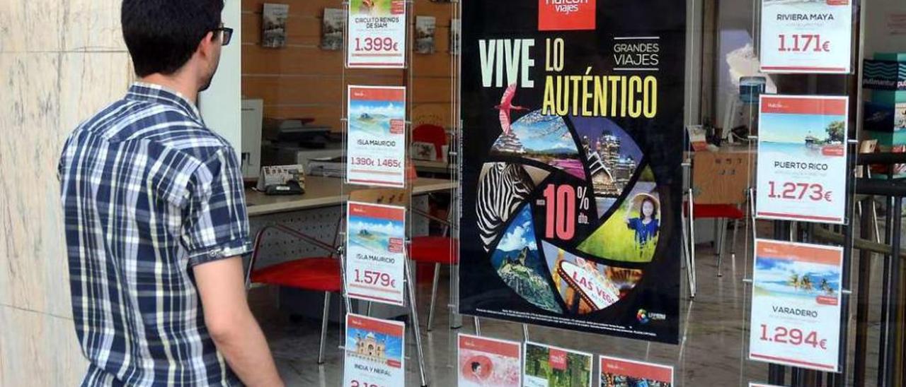 Un joven lee los carteles anunciadores de viajes exóticos de una agencia pontevedresa. // Rafa Vázquez