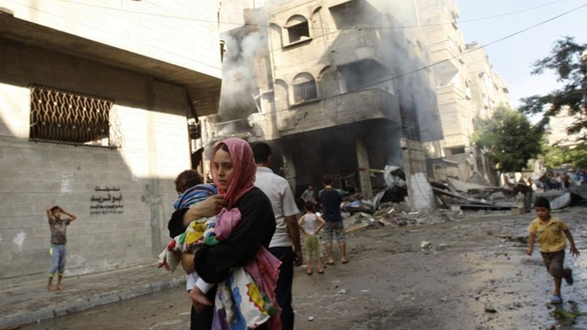 Una mujer palestina corre con su hijo para resguardarse de los ataques israelís, este jueves en Gaza.