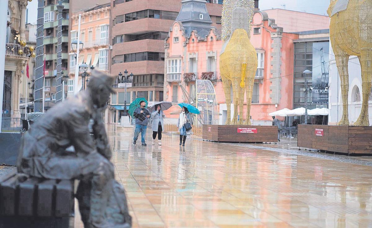 Un grupo paseando bajo la lluvia en las calles cercanas al puerto de Cartagena durante el día de Navidad.