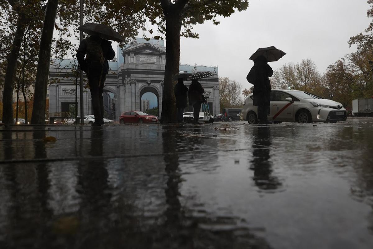 Varias personas se protegen con el paraguas de la lluvia en Madrid.