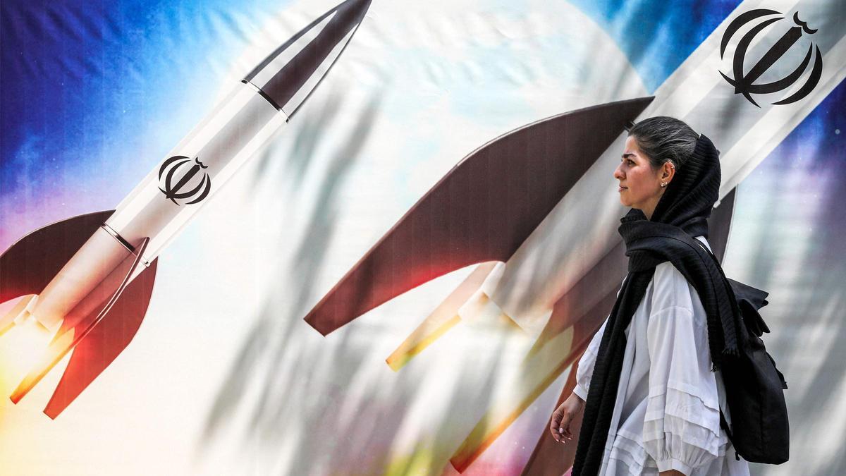 Una mujer pasa, en el centro de Teherán, junto a una pancarta que representa el lanzamiento de misiles con el emblema de la República Islámica de Irán.