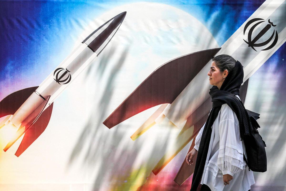 Una mujer pasa, en el centro de Teherán, junto a una pancarta que representa el lanzamiento de misiles con el emblema de la República Islámica de Irán.
