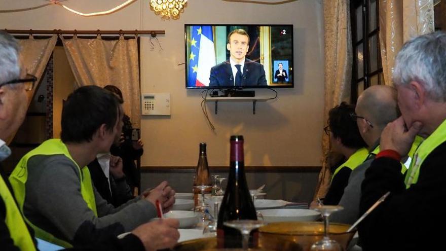 Varios personas siguen por televisión el mensaje de Macron.