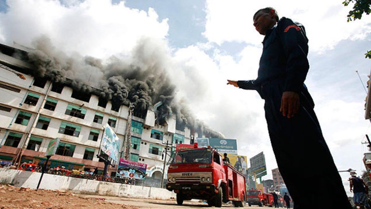 Un bomber de Myanmar assenyala un centre comercial en flames al centre de la ciutat de Yangon.