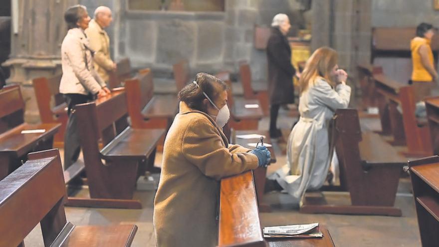 Una mujer con guantes y mascarilla, arrodillada durante una misa en una iglesia de Galicia.