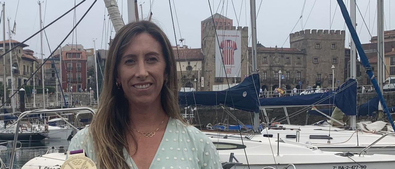 Ángela Pumariega, ayer, con la medalla en el puerto deportivo de Gijón. Arriba, la gijonesa, a la izquierda de Támara Echegoyen y Sofía Toro en el podio de Londres. | S. M. / Efe