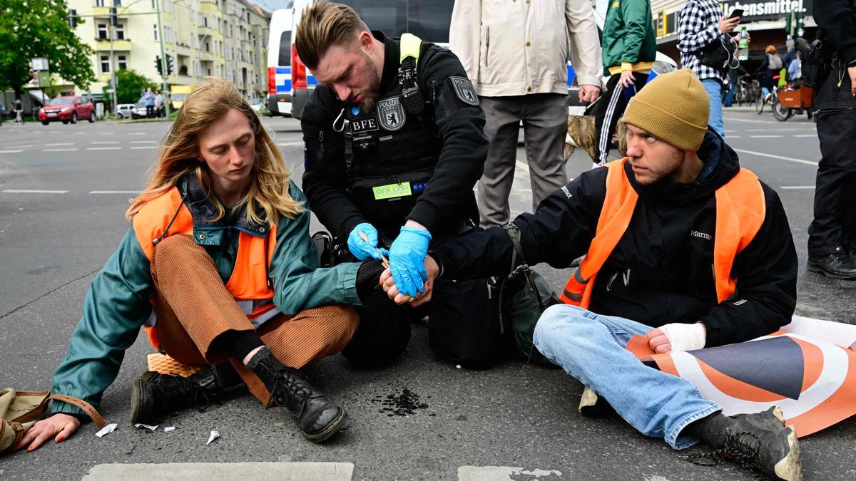 Un agente de policía intenta despegar del asfalto las manos de dos activistas enganchadas con pegamento durante un acto conta el cambio climático, el pasado 25 de abril en Berlín.