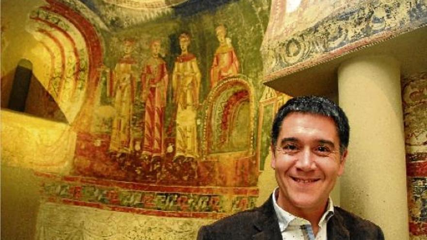 Martí Gironell mira a càmera davant les pintures de l&#039;església berguedana de Sant Quirze de Pedret, que conserva i exhibeix el MNAC