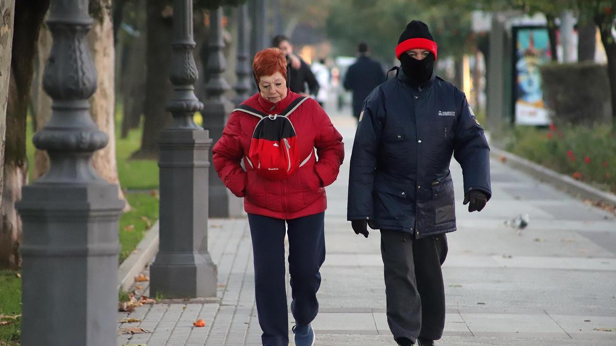 Dos personas caminan por Córdoba bien ataviados para hacer frente al frío.