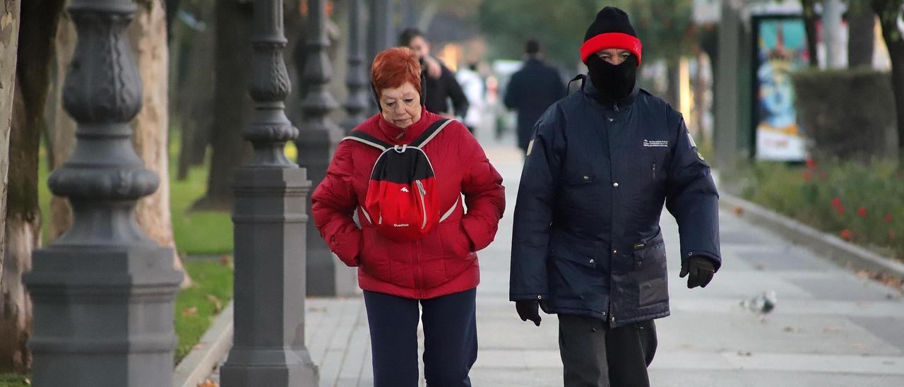 Dos personas caminan por Córdoba bien ataviados para hacer frente al frío.