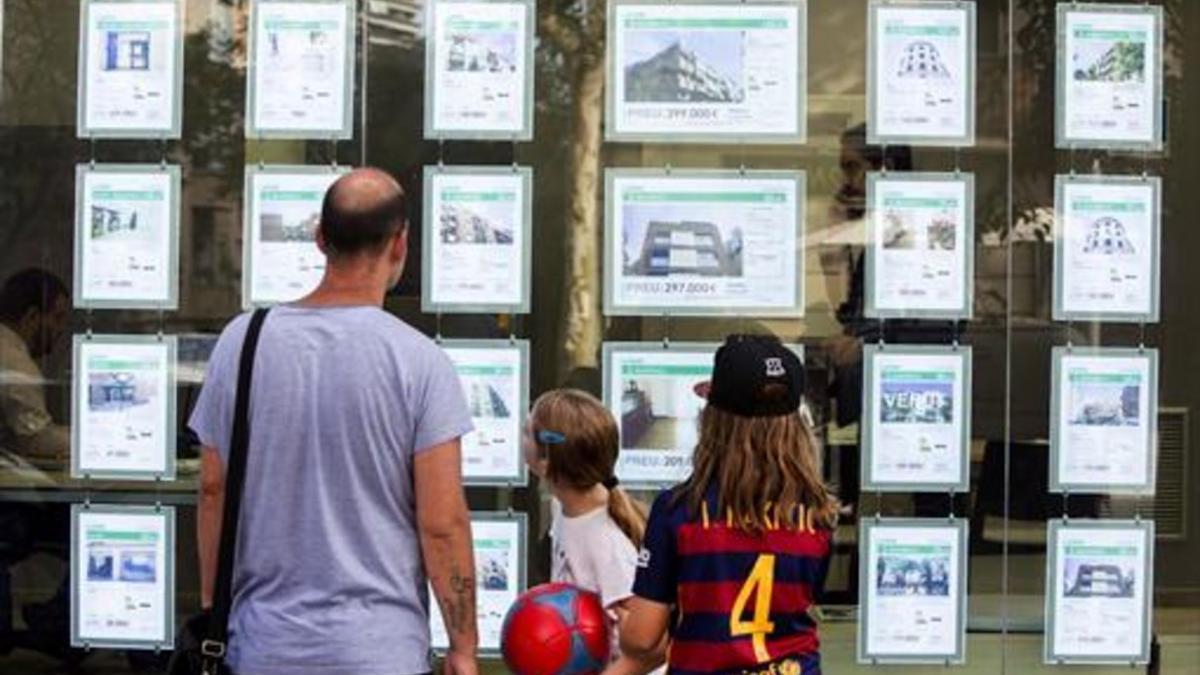 Un hombre y dos niñas observan las ofertas de viviendas en una agencia inmobiliaria del paseo de Maragall de Barcelona.