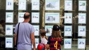 Un hombre y dos niñas observan las ofertas de viviendas en una agencia inmobiliaria del paseo de Maragall de Barcelona.