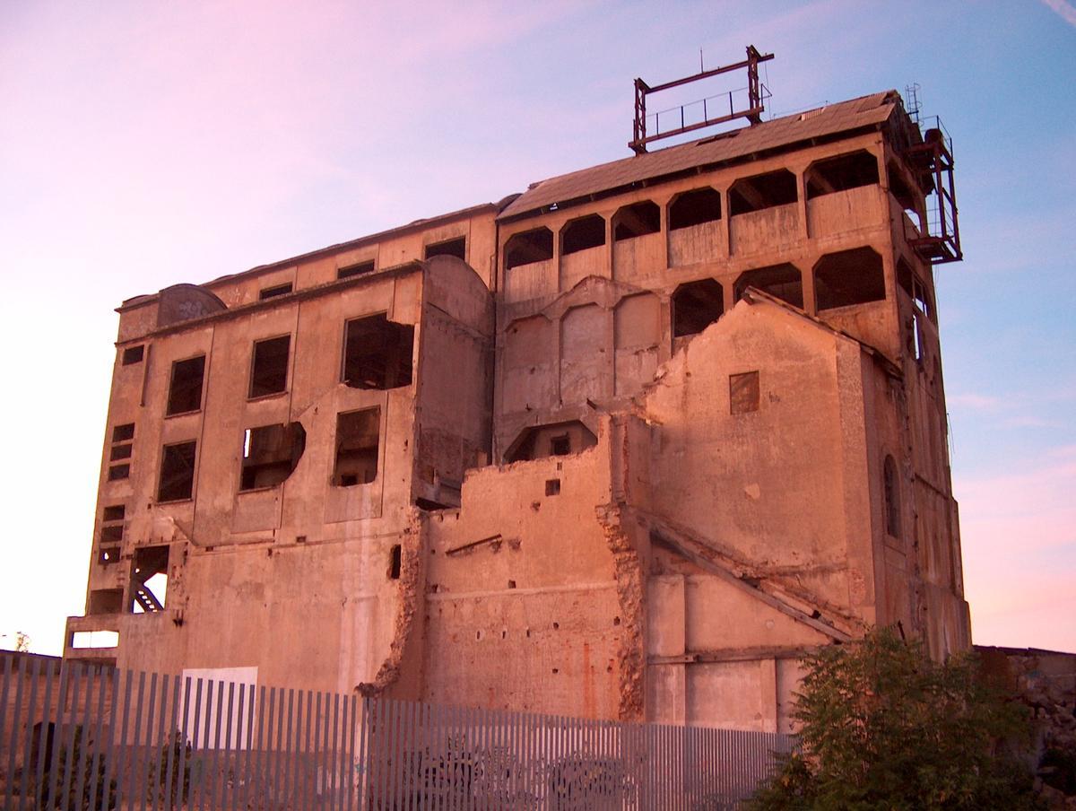 8. Molienda / Superfosfatos: Es el edificio más peculiar, ahora decrépito. La fosforita se elevaba a lo alto de la Fosa o Molienda para ir cayendo por machacadoras, cribas y molinos, a través de tolvas y embudos. Luego se enriquecía con el ácido sulfúrico creado en la fábrica aledaña. Los superfosfatos resultantes se repartían por el mundo.