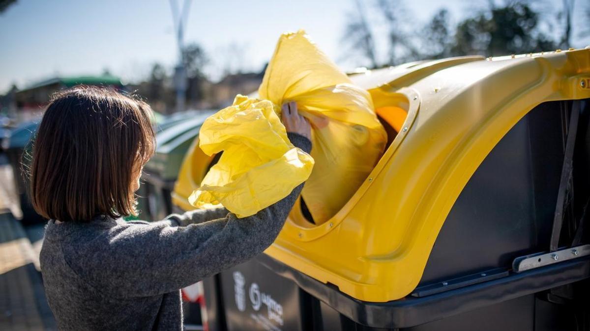 Una mujer deposita envases de plástico en el contenedor amarillo.