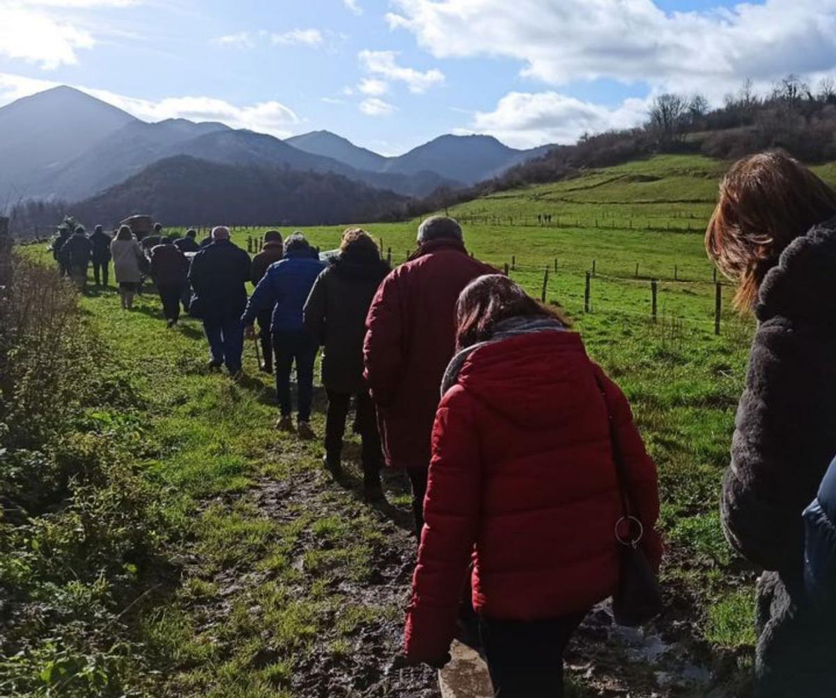 Familiares y vecinos inician el trayecto a pie hasta el camposanto, ubicado en la colina, a la derecha de la imagen. A la derecha, José Manuel García muestra el antiguo camino al cementerio. | S. Arias