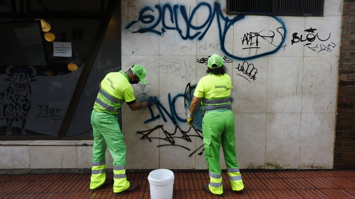 Dos empleados de limpieza trabajan para quitar un grafiti de una pared de Zaragoza