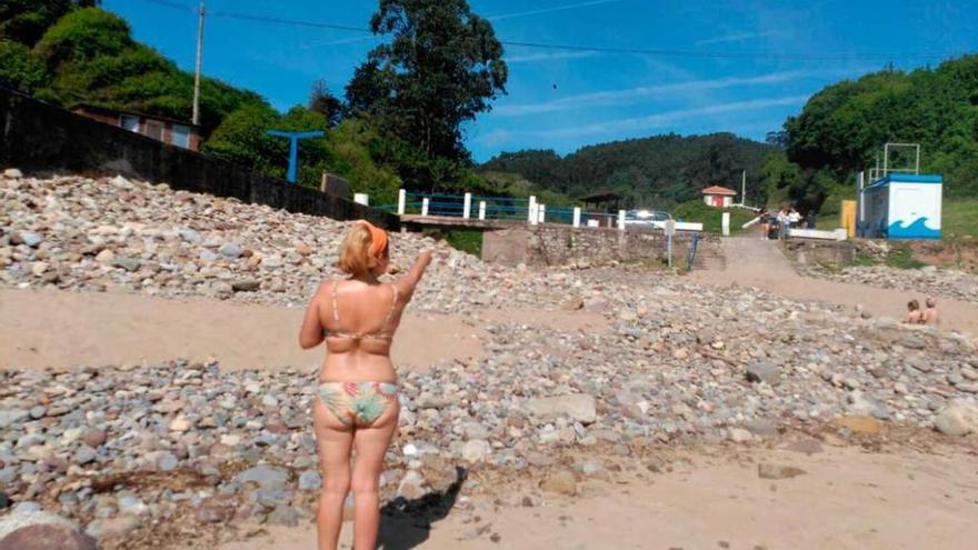 Una bañista señala hasta dónde llegan las piedras en la playa de El Astilleru, en Lastres.