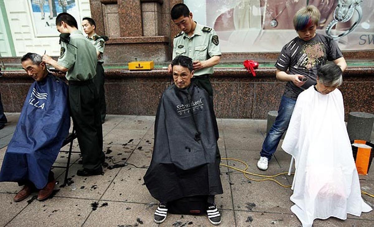 Dos soldats i un barber tallen els cabells gratis a uns homes grans en un carrer de Xangai (Xina) aquest divendres, dins un programa de serveis comunitaris de voluntaris destinat a ajudar la gent gran.