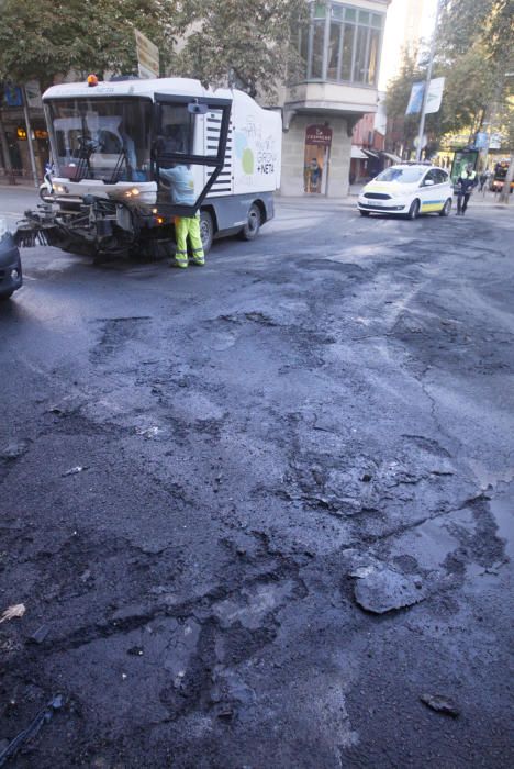 Carrers amb restes de mobiliari urbà cremat, contenidors per terra i treballadors de la brigada treballant