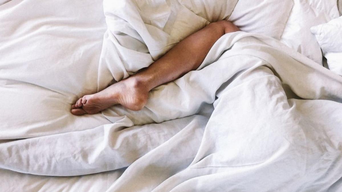 Imagen de un pie entre el edredón de la cama.