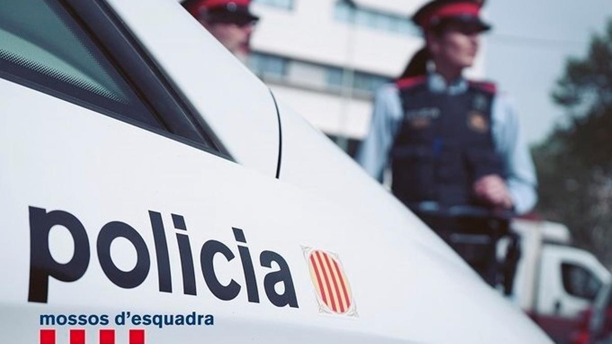 Una pareja de Mossos d'Esquadra, junto a un vehículo del cuerpo policial.