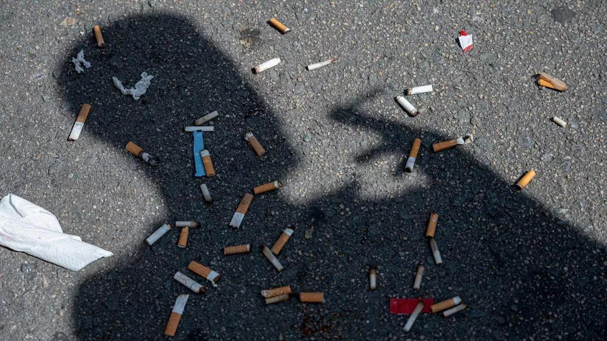 Sombra de un hombre fumando sobre un suelo lleno de colillas.