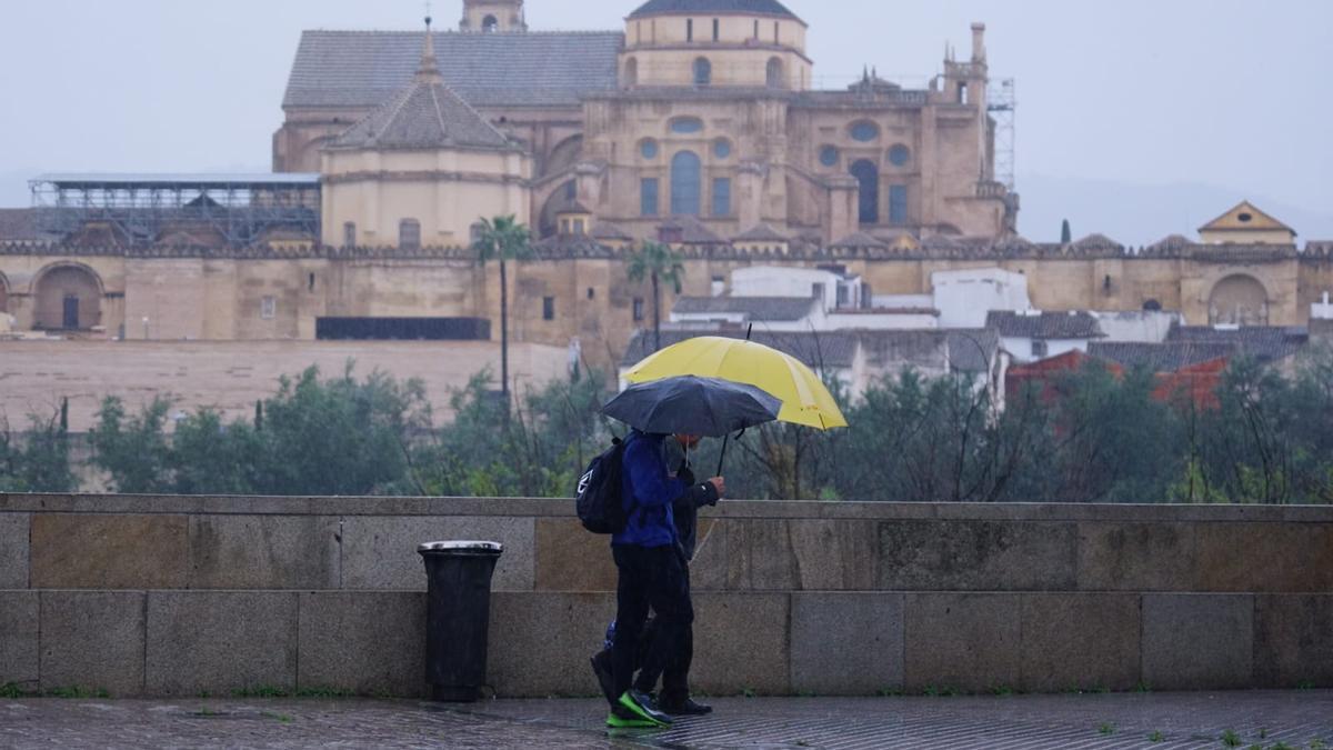 Viandantes se protegen de la lluvia en Córdoba, con la Mezquita-Catedral al fondo.