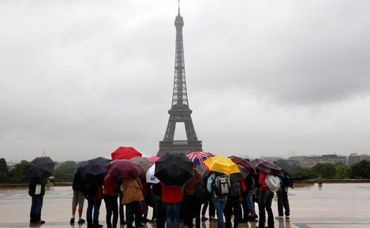 Els turistes es protegeixen de la pluja davant de la Torre Eiffel a París