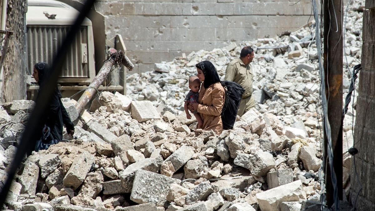 Una mujer iraquíe con un niño camina entre las ruinas de Mosul, un año después de la liberación de la ciudad