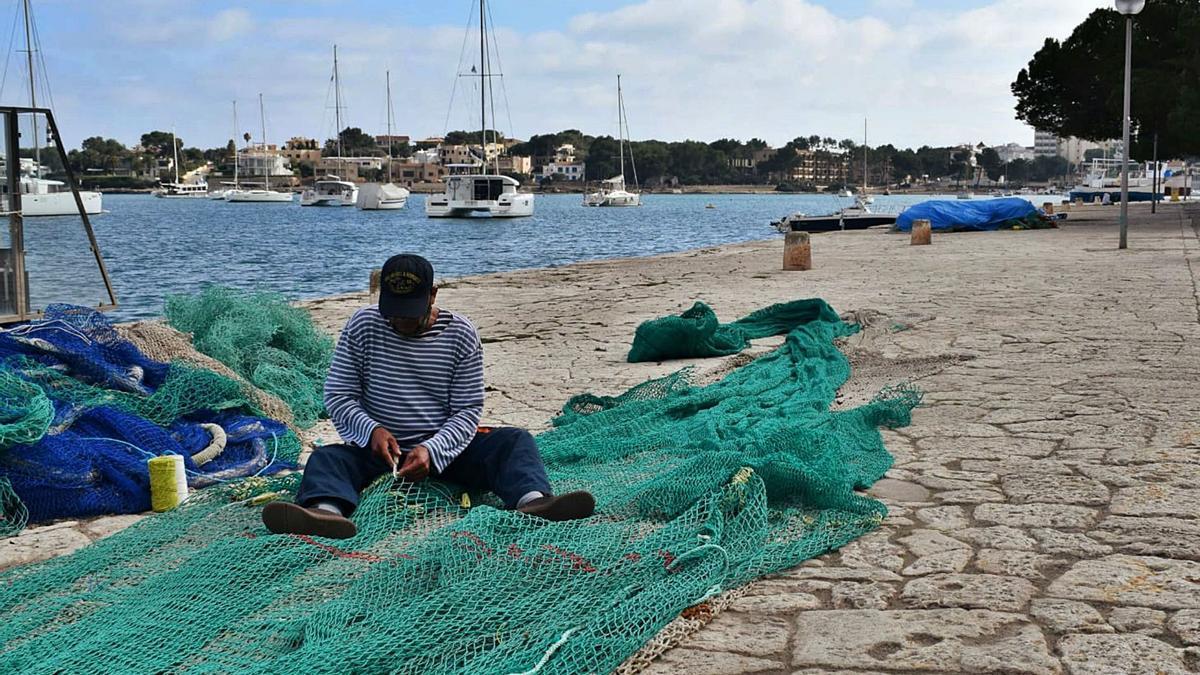 Un hombre arregla las redes de pesca sentado en medio del empedrado de sa Duana de Portocolom.