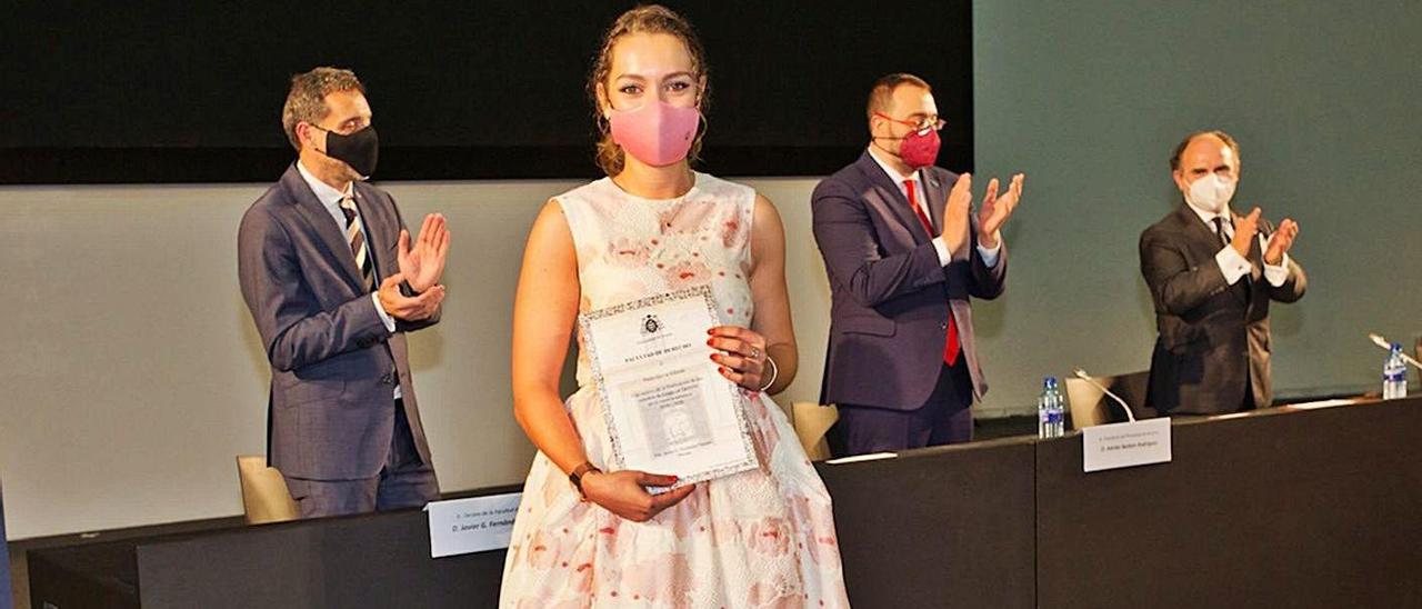 Una recién graduada en Derecho, ayer, con su diploma; detrás, el decano, Javier F. Teruelo; el presidente del Principado, Adrián Barbón, y el rector, Ignacio Villaverde.