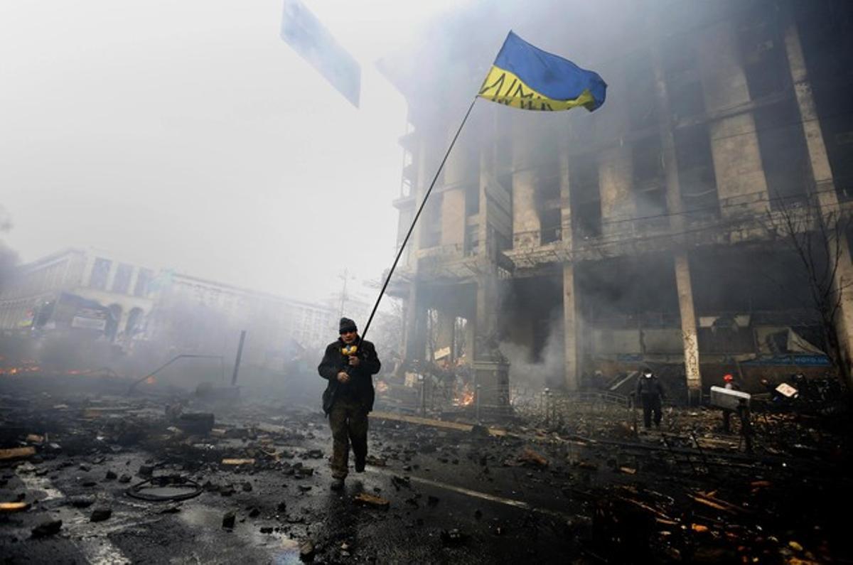 Un ciudadano lleva la bandera de Ucrania, entre las barricadas del centro de Kiev.