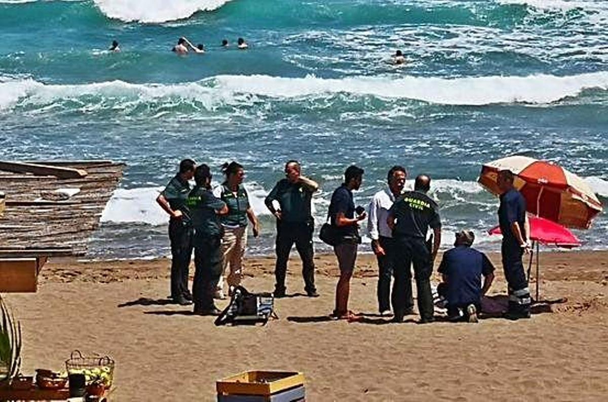 Els serveis de socorrisme, amb la víctima encara a la sorra, i al fons el mar amb fort onatge.