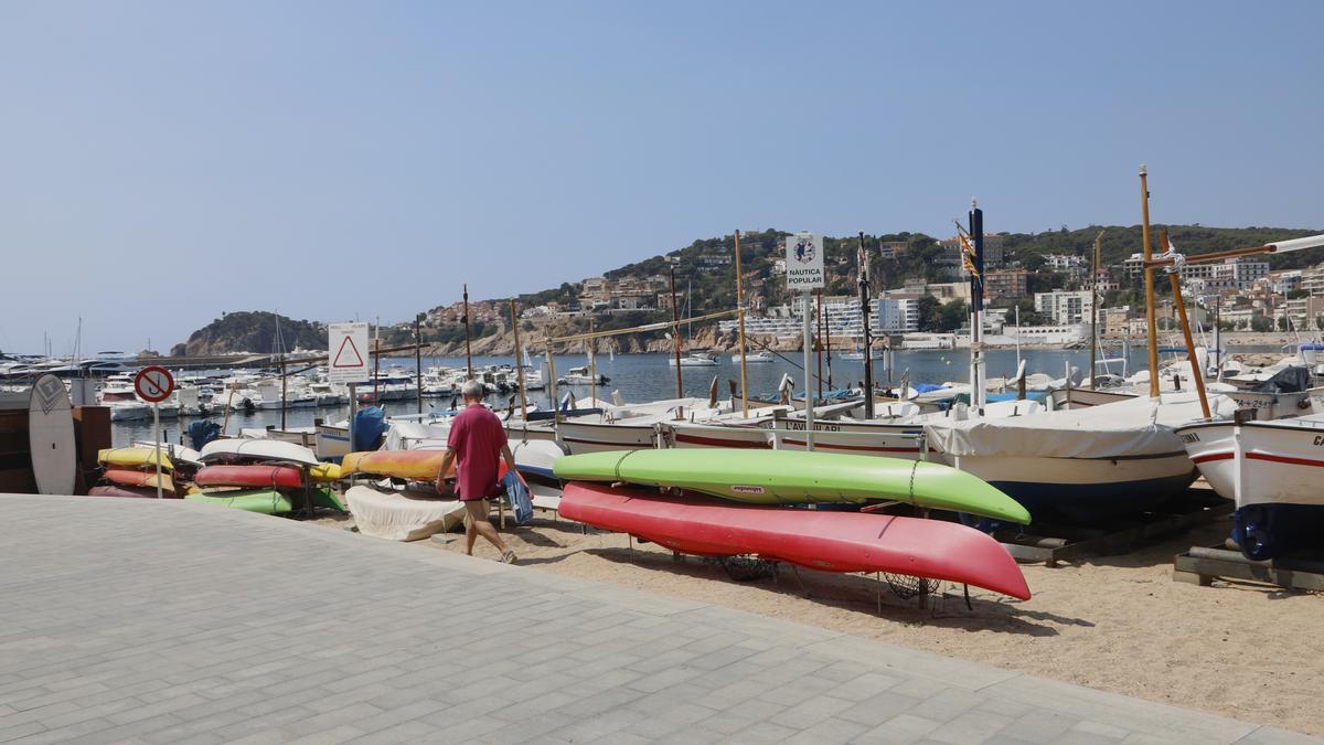 Un home passejant davant les barques del club nàutic popular Llop de Mar de Sant Feliu de Guíxols