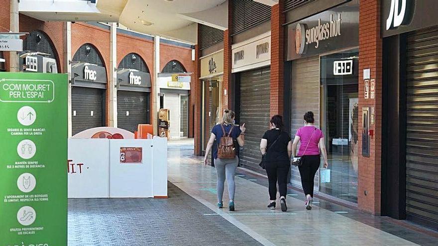 Tres clientes, al fons, passejant ahir per l&#039;Espai Gironés, amb un dels cartells amb les normes de seguretat i higiene en primer pla.