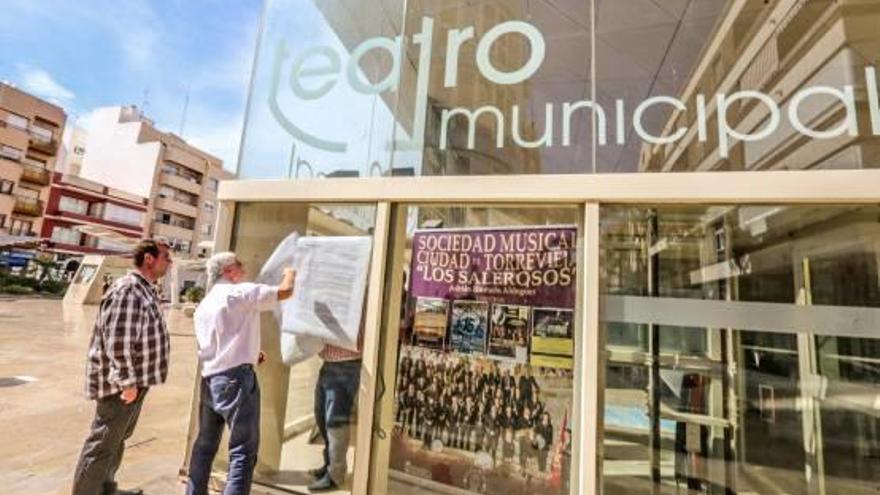 Colocación de los carteles en la fachada acristalada del Teatro Municipal.