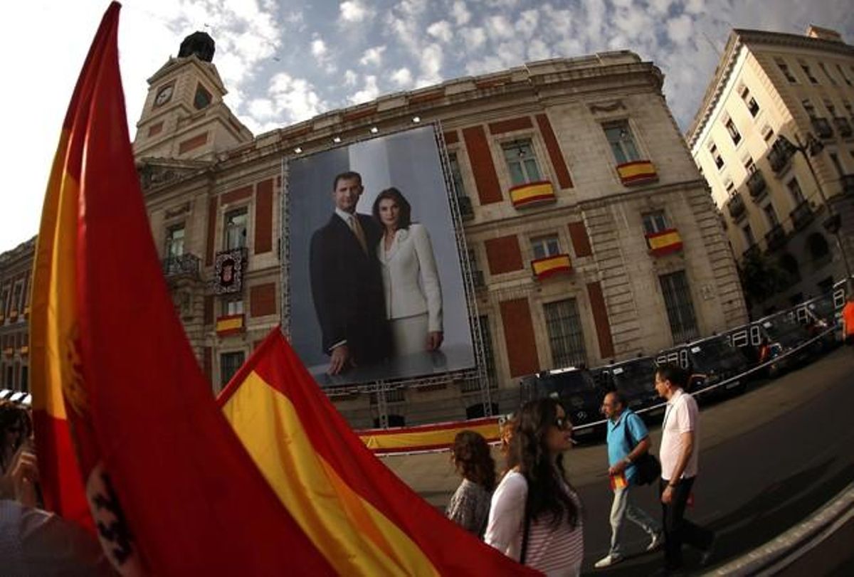 Les persones amb banderes espanyoles passen al costat d’una imatge que mostra el nou rei Felip VI i la seva dona, la reina Letizia.