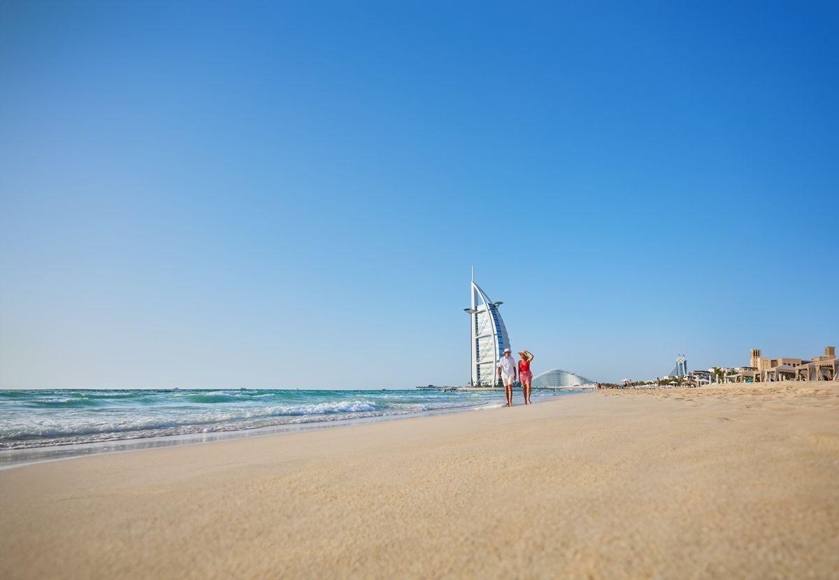 Una pareja disfrutando de un tranquilo paseo por la playa con las impresionantes vistas de Dubái como telón de fondo.
