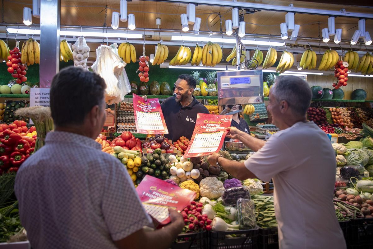 Joan Marí y Alex Minchiotti entregan un par de calendarios en un puesto del Mercat Nou.