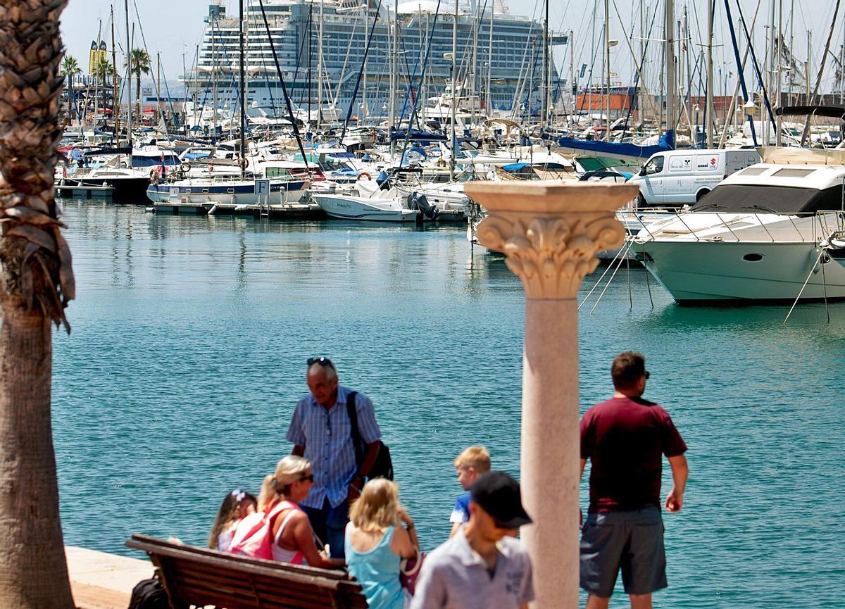 Turistas en el paseo del puerto de Alicante. Al fondo, uno de los dos cruceros que ha hecho escala este  julio.  | JOSE NAVARRO